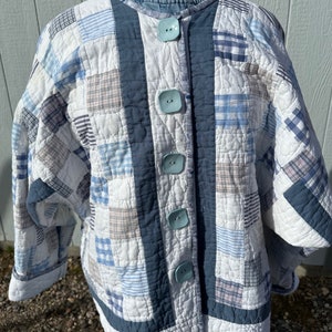 May include: A white quilted jacket with blue and white plaid patchwork. The jacket has a blue trim and blue buttons.