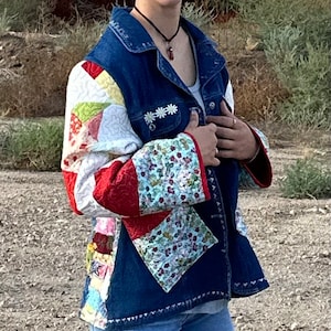 May include: A blue denim jacket with patchwork quilt sleeves. The sleeves are made of a variety of fabrics in red, white, green, and yellow. The jacket has a white flower design on the left side of the chest.