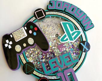 Könnte beinhalten: Lila und türkisfarbener Tortendekor mit einem Videospiel-Controller, einem PlayStation-Logo und dem Text "Jordyn Level 10".