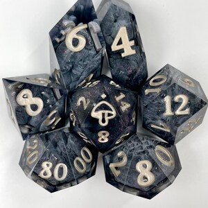 May include: A set of seven polyhedral dice made of dark, smoky resin with swirling gray and black patterns and fine glitter. The numbers are inlaid in a metallic silver color. The twenty-sided die features a small mushroom icon on the top face.