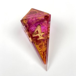 May include: A four-sided polyhedral die featuring a translucent resin body with swirling magenta and metallic gold pigments. The number four is prominently displayed on the front face in a raised, gold-colored font with a serif typeface.
