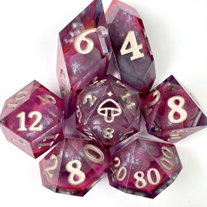 May include: A set of seven polyhedral dice made of translucent resin with a deep red and purple swirl pattern containing silver glitter. The dice feature silver-colored numbers and a mushroom icon on the twenty-sided die, arranged in a cluster.