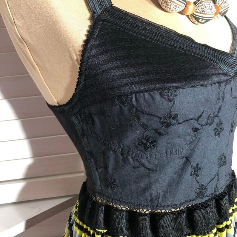May include: Black halter top dress with floral embroidery and a pleated skirt. The bodice features a V-neckline and delicate lace trim. The skirt has yellow and blue accents.