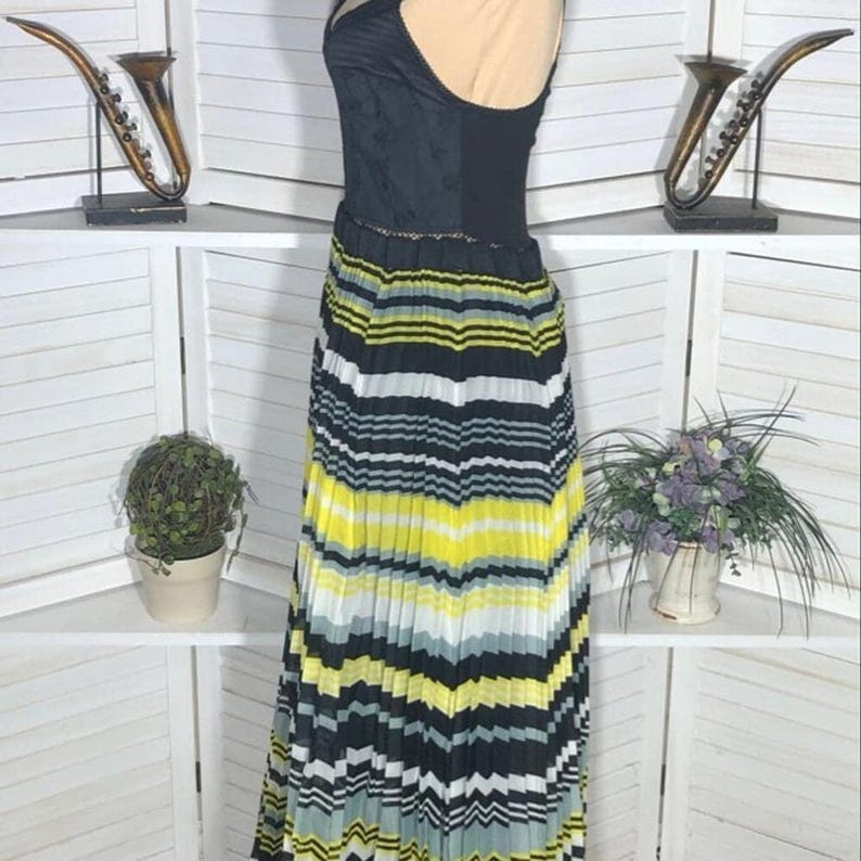 May include: A black and yellow striped maxi dress with a black bodice. The dress features a pleated skirt with horizontal stripes in black, yellow, white, and gray. The bodice has a textured pattern.