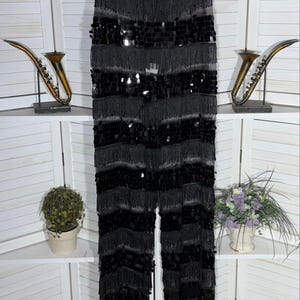 May include: Black fringed pants with sequin accents. The pants have a wide leg design and are made of a soft, flowing material. The pants are hanging on a hanger against a white background.