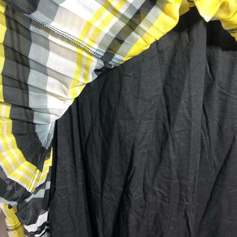 May include: A pleated skirt with a black lining and a yellow, white, and gray plaid pattern. The skirt's fabric is lightweight and appears to be semi-sheer, with a visible seam at the waist.