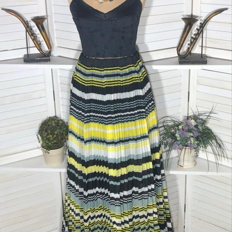 May include: A black dress with a pleated skirt featuring horizontal stripes in yellow, black, white, and gray. The bodice is black with a V-neck and a subtle floral pattern. A thin belt accents the waist.