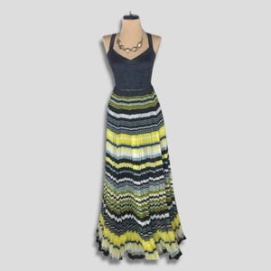 May include: A black halter-neck dress with a pleated, striped skirt in yellow, black, and white. The dress is displayed on a mannequin with a gold-toned necklace. The bodice has a subtle polka-dot pattern.