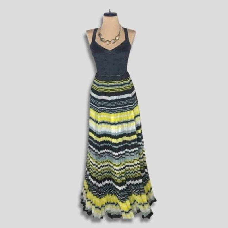 May include: A black halter-neck dress with a pleated, striped skirt in yellow, black, and white. The dress is displayed on a mannequin with a gold-toned necklace. The bodice has a subtle polka-dot pattern.