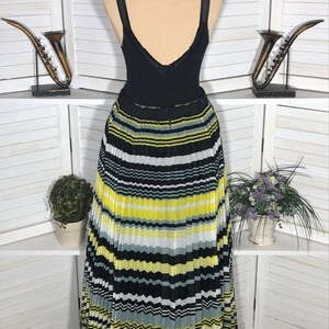 May include: A black sleeveless top with a V-neck is paired with a pleated skirt. The skirt features horizontal stripes in yellow, white, black, and gray. The dress is displayed on a mannequin.
