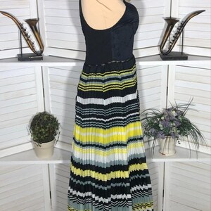 May include: A sleeveless dress with a black bodice and a pleated skirt. The skirt features horizontal stripes in black, white, yellow, and gray. The dress is displayed on a mannequin.