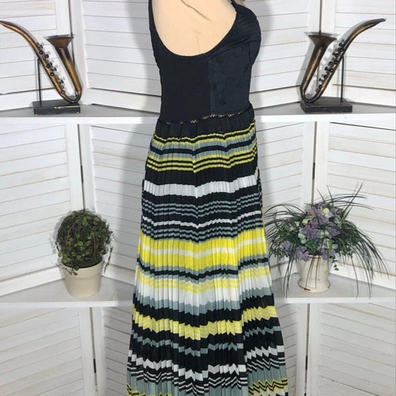 May include: A sleeveless dress with a black bodice and a pleated skirt. The skirt features horizontal stripes in black, white, yellow, and gray. The dress is displayed on a mannequin.