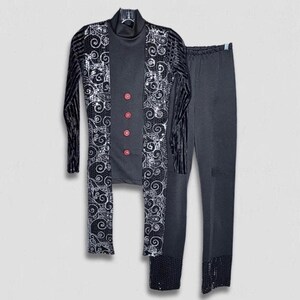 May include: A black dance costume set. The set includes a long-sleeved top with a high collar and red buttons, a long jacket with a black and silver swirl design, and matching pants. The jacket has black velvet stripes on the sleeves.