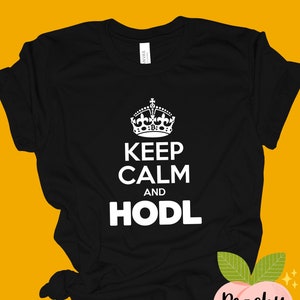 May include: Black t-shirt with a white crown and the text "Keep Calm and HODL". The shirt is folded and has a peach-colored tag with the text "Peachy Tee" on it.