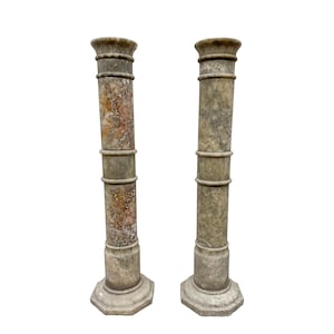 May include: Two antique marble columns with a weathered appearance. The columns are cylindrical with decorative bands and a detailed capital. The bases are hexagonal. The color is a mix of grey, beige, and hints of reddish-brown.