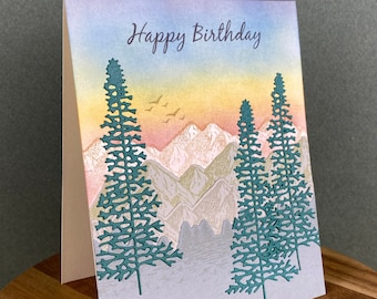 May include: A greeting card with a watercolor background of mountains and trees. The text "Happy Birthday" is printed in purple at the top of the card.