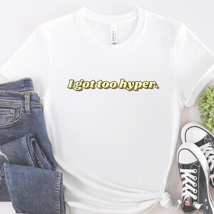 May include: White t-shirt with the text "I got too hyper." in yellow letters with a brown outline.