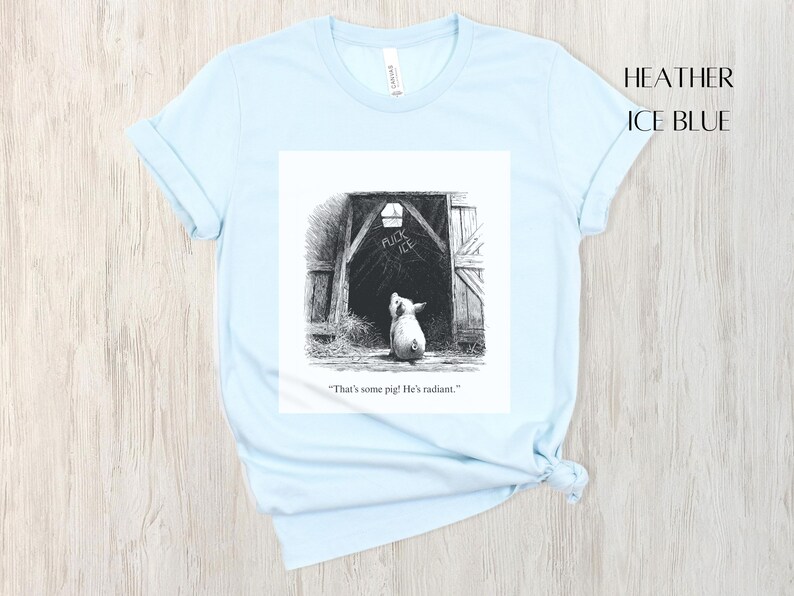 Puede incluir: Camiseta azul claro con una ilustraci&oacute;n en blanco y negro de un cerdo mirando hacia un granero. La ilustraci&oacute;n incluye el texto "That's some pig! He's radiant."