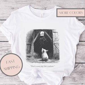 Puede incluir: Camiseta blanca con una ilustraci&oacute;n en blanco y negro de un cerdo mirando hacia la entrada de un granero. El texto "FUCK ICE" est&aacute; encima de la entrada. La cita "That's some pig! He's radiant." est&aacute; debajo.
