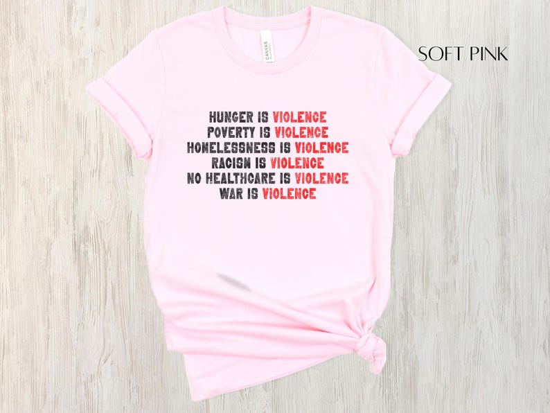 May include: Pale pink t-shirt featuring the statement "HUNGER IS VIOLENCE, POVERTY IS VIOLENCE, HOMELESSNESS IS VIOLENCE, RACISM IS VIOLENCE, NO HEALTHCARE IS VIOLENCE, WAR IS VIOLENCE" in black and red text.