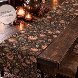 May include: A long table runner featuring a dark background with a repeating botanical pattern of orange persimmon fruits, green leaves, and small white flowers. The text Persimmon Table Runner is printed in the upper left corner.