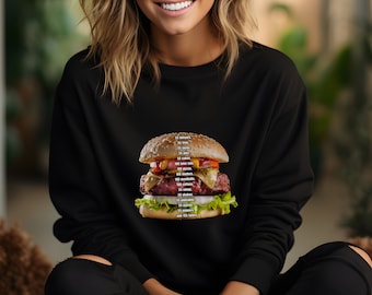 May include: A black long-sleeve sweatshirt featuring a graphic of a large cheeseburger. The burger is layered with lettuce, onion, cheese, and a patty, with a list of food items printed in white text directly over the center of the burger image.
