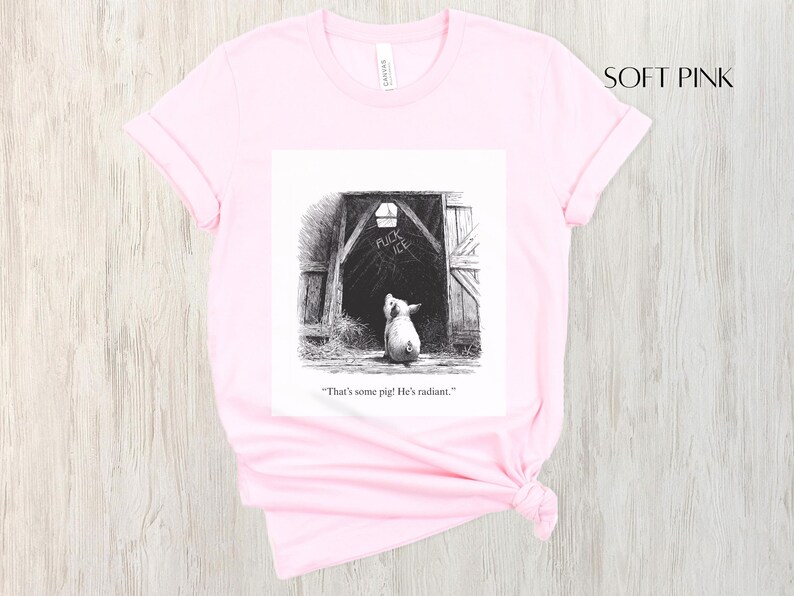 Puede incluir: Camiseta rosa claro con una ilustraci&oacute;n en blanco y negro de un cerdo mirando una puerta de granero. El texto de la ilustraci&oacute;n dice: "That's some pig! He's radiant."