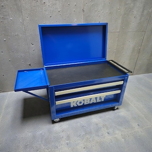 May include: A blue rolling tool chest with a hinged top and two drawers. The chest has a pull-out side tray and a black work surface. The brand name "KOBALT" is displayed on the front of the drawers.