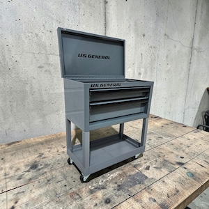 May include: Gray rolling tool chest with the lid open. The chest has multiple drawers and a bottom shelf. The text "U.S. GENERAL" is printed on the lid and the front of the chest.