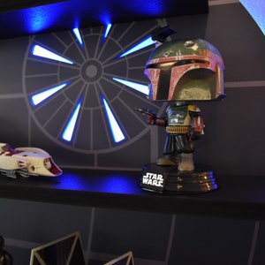 Op de afbeelding: Een Star Wars-thema plank met een Boba Fett Pop-figuur, een ruimteschip en een blauw licht erachter.