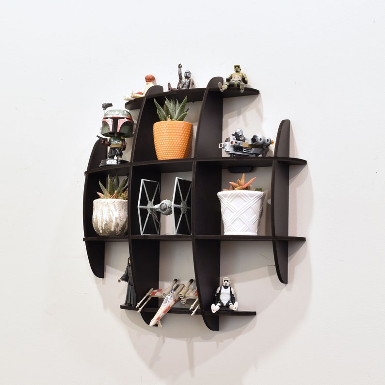 May include: A black wall shelf shaped like the Death Star from Star Wars. The shelf has multiple compartments and is decorated with small figurines and potted plants.