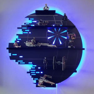 Op de afbeelding: Een zwart Death Star-vormig rek met blauwe LED-verlichting. Het rek heeft vier niveaus en is versierd met Star Wars-figuurtjes en voertuigen. De figuurtjes omvatten een Stormtrooper, een Boba Fett, een Darth Vader en een Rebel-piloot. De voertuigen omvatten een TIE-jager, een X-wing en een speeder.