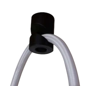 May include: Black cord holder for hanging a lamp or light fixture. The holder is made of plastic and has a round shape. It is designed to hold a cord securely in place.