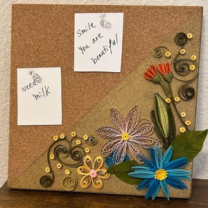 Può includere: Bacheca in sughero con fiori di carta arrotolata rosa, blu e gialli. Due note sono appuntate sulla bacheca, una con scritto "Need milk" e l'altra "Smile You are beautiful". La bacheca ha un design triangolare.