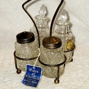 May include: Vintage silver-plated salt and pepper shaker set. The set includes four clear glass bottles with diamond-patterned sides, held in a metal stand. The bottles have metal lids and crystal-like stoppers. A blue tag reads "Tales of Sheffield".