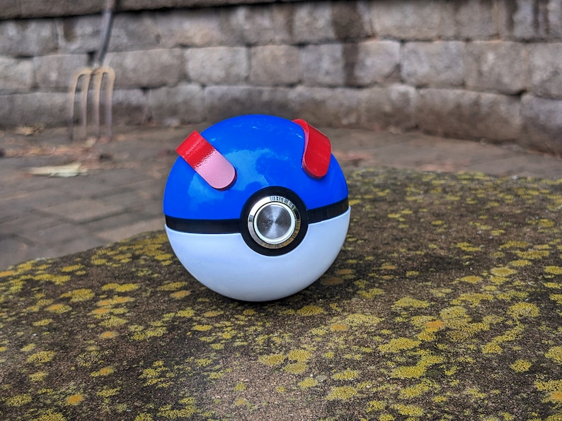 May include: A blue and white Poke Ball with red accents. The ball has a black ring around the middle and a silver button in the center.