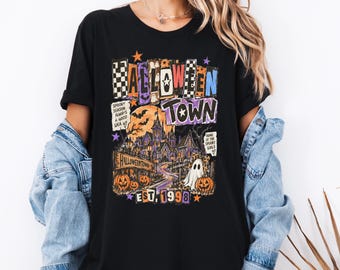 May include: A black t-shirt featuring a graphic print with the text HALLOWEEN TOWN EST. 1998. The design includes a haunted house, a large orange moon, pumpkins, a ghost, and smaller text reading SPOOKY SEASON ALWAYS A GOOD IDEA.