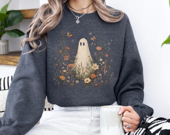 May include: A dark charcoal gray crewneck sweatshirt featuring a central graphic of a cream-colored ghost surrounded by various orange, yellow, and brown wildflowers, foliage, and small butterflies, with long sleeves and a ribbed neckline.