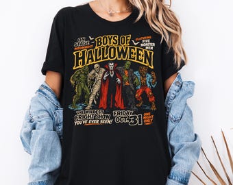 May include: A black t-shirt featuring a graphic print of five classic monsters standing together. The text reads: ON STAGE MIDNIGHT BOYS OF HALLOWEEN FEATURING FIVE MONSTER MEN THE WILDEST FRIGHT SHOW YOU'VE EVER SEEN! FRIDAY OCT. 31 ONE NIGHT ONLY.