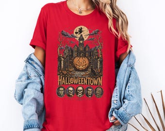 May include: A red short-sleeve t-shirt featuring a graphic print of a haunted mansion, a large jack-o'-lantern, a witch on a broomstick, and the text HALLOWEENTOWN above five circular portraits of classic horror movie monsters.