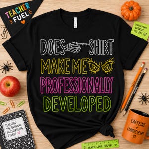 Op de afbeelding: Een zwart t-shirt met korte mouwen en witte, gele, roze en limoengroene tekst met de tekst DOES SHIRT MAKE ME PROFESSIONALLY DEVELOPED. Het ontwerp bevat een witte skelet hand die wijst en gele gestileerde ogen boven de tekst.