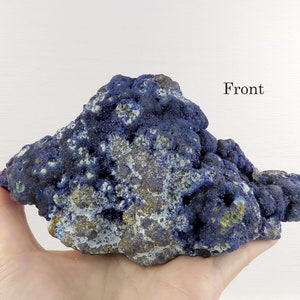 Könnte beinhalten: Ein großes, blaues und grünes Azurite-Mineralienstück mit einer rauen, strukturierten Oberfläche. Das Mineral wird auf einer Hand gezeigt, mit dem Wort "Front" in schwarzer Schrift darüber.