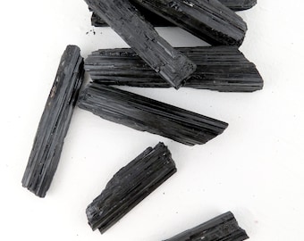 Könnte beinhalten: Sechs schwarze Turmalin-Stäbe, auch bekannt als Schörl, auf weißem Hintergrund. Die Stäbe sind unterschiedlich lang und haben eine raue, natürliche Textur.