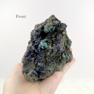 Könnte beinhalten: Ein rauer, dunkelgrauer Stein mit grünen und blauen Kristallen. Der Stein ist etwa so groß wie eine menschliche Hand. "Front" steht in schwarzer Schrift oben im Bild.