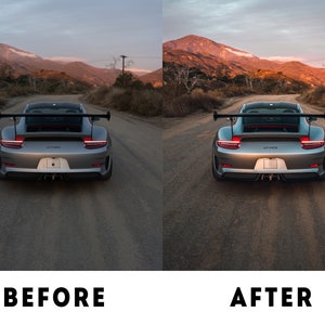 May include: A silver Porsche 911 GT3 RS with a black rear wing and red tail lights is parked on a paved road. The car is facing away from the camera. The background is a mountain range with a sunset sky.
