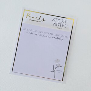 May include: A white sticky note pad with gold trim and the text "Pearls of Parchment" at the top. The pad includes the text "STICKY NOTES" and "50 SHEETS". The pad also has a floral illustration and a bible verse.