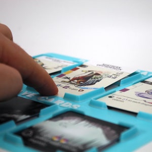 Può includere: Un porta carte in plastica blu con fessure per contenere le carte. Le carte presentano illustrazioni di creature fantastiche e un testo che dice "Serpente Fantastico" e "Serpente del Cielo".