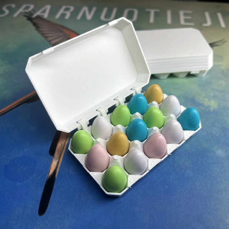 May include: A white plastic egg carton with a lid, filled with pastel coloured plastic eggs. The eggs are in shades of blue, green, pink, and yellow.