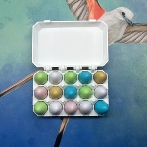 May include: A white plastic egg carton with a hinged lid, filled with 18 pastel-coloured plastic eggs. The eggs are in shades of green, blue, and pink.