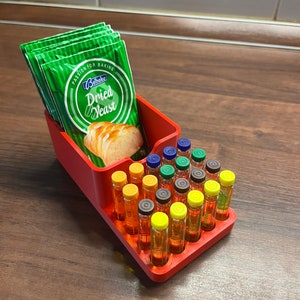 Könnte beinhalten: Roter Plastik-Organizer mit einem Fach für Trockenhefe-Päckchen und einem Raster mit Schlitzen für kleine Glasfläschchen. Die Hefepäckchen sind grün und haben den Text "Belbake Dried Yeast" aufgedruckt. Die Fläschchen sind mit einer klaren Flüssigkeit gefüllt und haben farbige Kappen.
